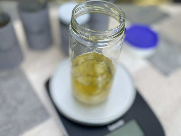 Ölauszug Ein Glasgefäß mit einer gelblichen Flüssigkeit auf einer digitalen Waage.