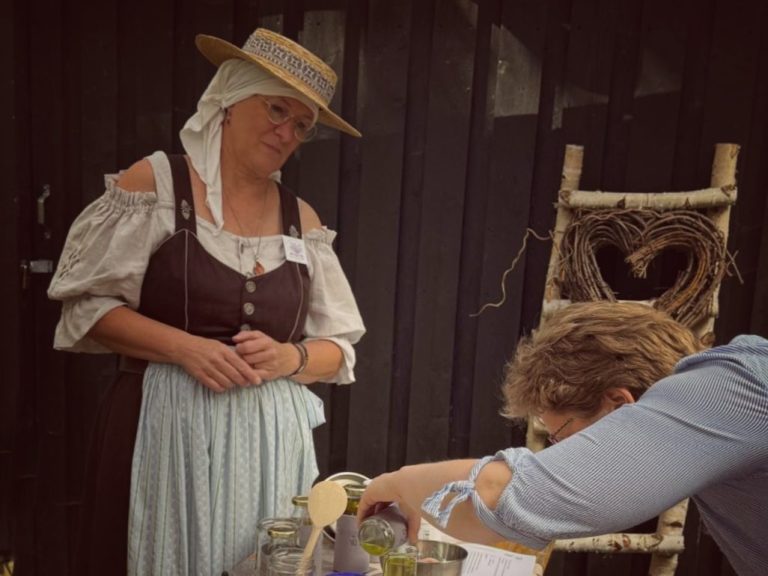 im Workshop Frau in historischer Kleidung steht neben einem Tisch mit Essen und einem Stuhl im Hintergrund.